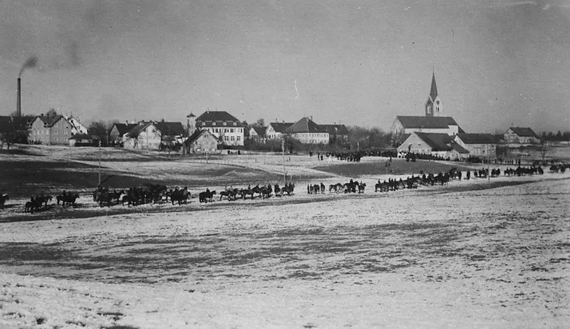 Historische Aufnahme: langer Reiterzug auf verschneiten Feldern vor Eisenharz, im Hintergrund der Kirchturm