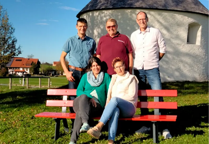 Die Vorstandschaft der Stephansreitergruppe auf einer roten Bank vor der Stephanskapelle